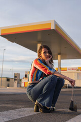 chica con camisa de colores y pelo largo sentada enfrente de una gasolinera mirando a la cámara