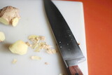 Fototapeta Tulipany - Ginger is being sliced on a plastic chopping board with a knife on an orange table.