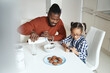 © Svitlana - African American man making breakfast for his daughter while she playing on the smartphone