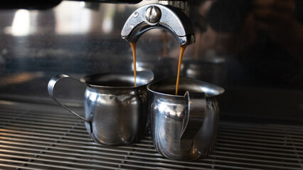 coffee machine dripping coffee into two metal cups 