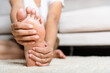 © sorapop - Foot pain, Asian woman feeling pain in her foot at home, female suffering from feet ache use hand massage relax muscle from soles in home interior, Healthcare problems and podiatry medical concept
