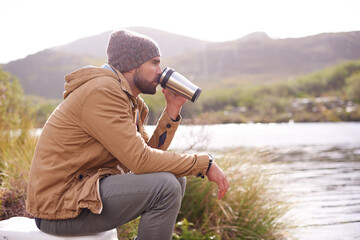 Sticker - Enjoying the scenery. Shot of a handsome man sitting by a lake drinking from a thermos.