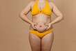 © Юля Бурмистрова - Cropped image of overweight fat naked woman with obesity, excess fat in yellow swimsuit. Adipose. Holding stomach flabs, visceral, cellulite. Self acceptance, body positive, plus size, friable skin