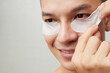 © DragonImages - Close-up image of smiling young man applying patches to brighten and reduce dark circles under eyes