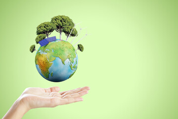 Poster - Close up of female hand holding creative globe with trees and solar panels on green background with mock up place. Energy and sustainable concept.