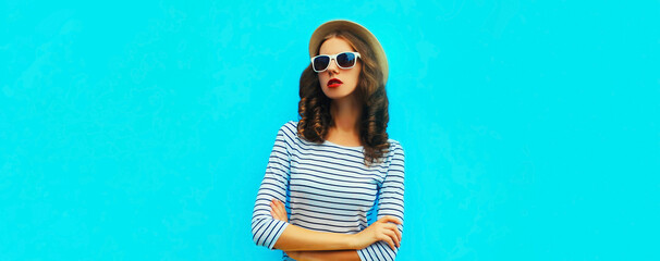 Portrait of stylish young woman model posing wearing a striped t-shirt and summer straw round hat on blue background