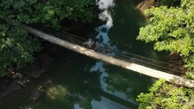 Beautiful Suspended Wood Bridge Over A Green River, Quiet Place In The Nature Of Costa Rica. Aerial Top Shot Of An Adventure Place, In The Wild Forest.