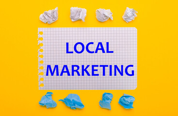 On a yellow background, white and blue crumpled pieces of paper and a notebook with the text LOCAL MARKETING