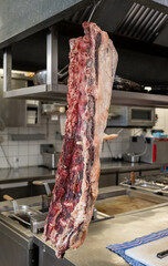 Wall Mural - Großes Dry Aged Rippe Steak wird von einem Koch in der Küche mit einem Messer zerlegt und bearbeitet 