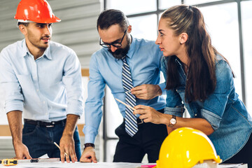 Professional of team architect industrial engineer cargo foreman in helmet working new construction project architectural plan with blueprint and construction tool at the building construction site