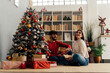 © Westend61 - Happy woman with boyfriend holding gift box sitting by Christmas tree at home