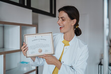 Happy Female Doctor Holding Certificate In Clinic