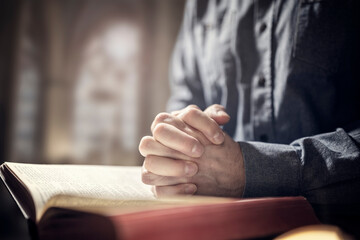 Hands folded in prayer on a Holy Bible in church, faith, spirtuality and religion