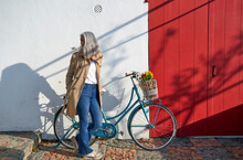 Woman With Bicycle Standing In Front Of Wall On Sunny Day
