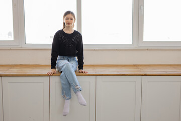 Wall Mural - caucasian teen girl sitting near a big window 