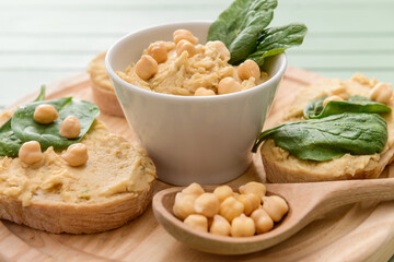 Board with pieces of bread and tasty hummus on table