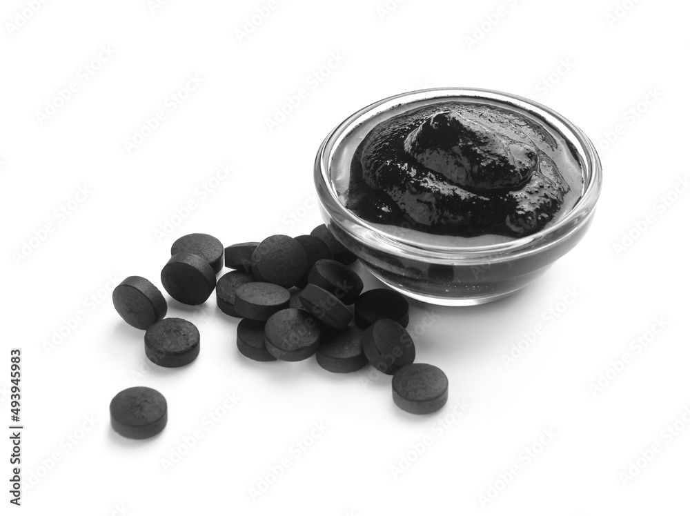 Bowl of activated carbon mask and pills on white background