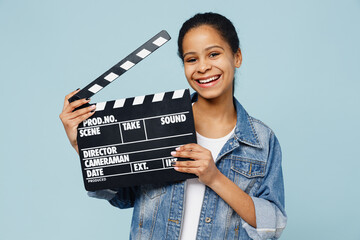 Wall Mural - Little fun kid teen girl of African American ethnicity 12-13 years old in denim jacket holding classic black film making clapperboard isolated on pastel plain light blue background. Childhood concept.