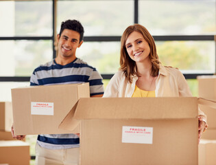 Canvas Print - Heres to new beginnings.... Portrait of a smiling young couple carrying boxes on moving day.