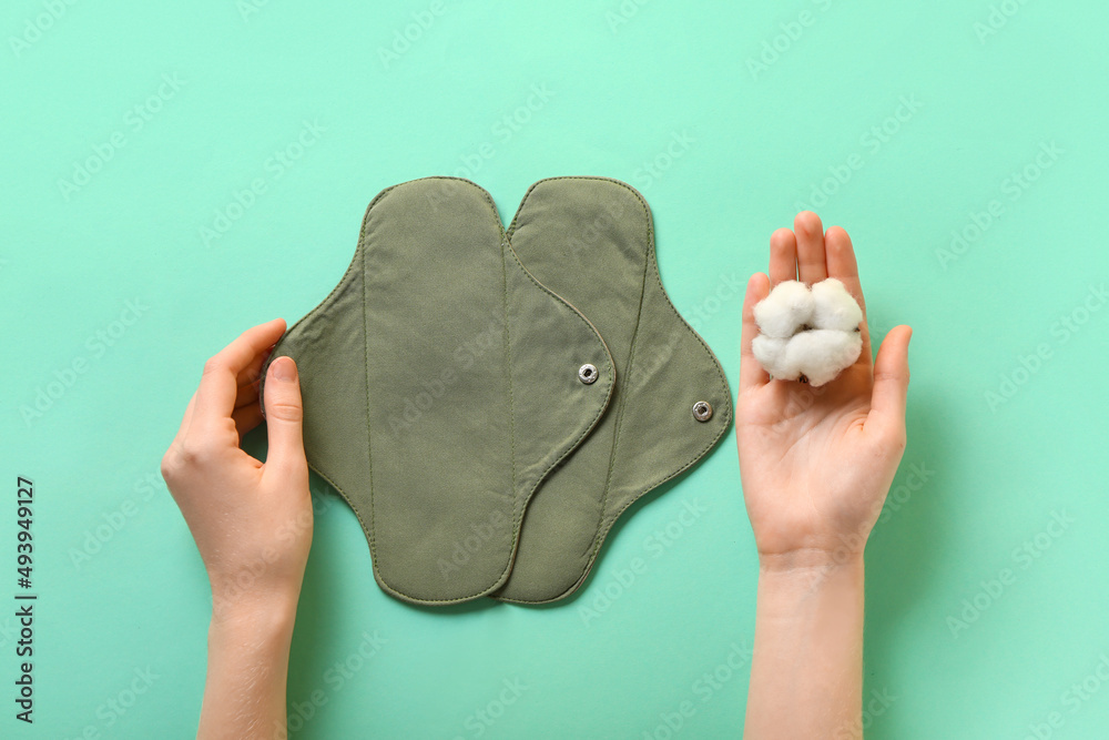 Female hands with reusable menstrual pads and flower on green background