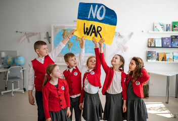 Wall Mural - Little schoolchildren holidng and showing ukrainian flag in classroom, no war concept.