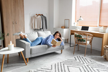 Wall Mural - Beautiful woman with book resting on couch at home