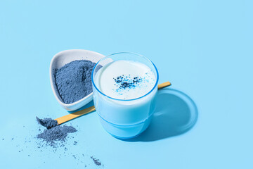 Glass of delicious matcha tea, bowl and chashaku with powder on blue background