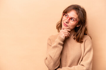 Young caucasian woman isolated on beige background relaxed thinking about something looking at a copy space.