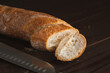 Cut into pieces fresh loaf of wheat bread. Slices of french baguette and knife on wooden table