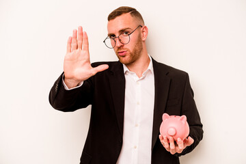 Young business caucasian man holding piggy bank isolated on white background standing with outstretched hand showing stop sign, preventing you.