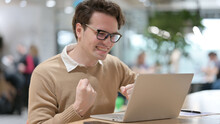 Young Man With Laptop Celebrating In Office 