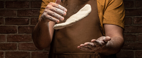 Pizza dough, male hands making dough with flour in a freeze motion of a cloud of flour midair on black with copy space, Long banner format