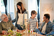 © KAMPUS - Happy siblings talking to grandpa and father at family dinner. Smiling teenage girl and preteen boy standing at dinner table having conversation with relatives. Family party, event concept