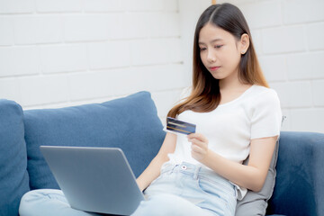 Wall Mural - Young asian woman sit on sofa using laptop computer shopping online with credit card buying to internet, happy girl payment with e-business on couch, purchase and payment, business concept.