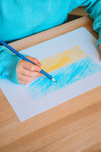 A Small Child Draws The National Flag Of Ukraine In Yellow And Blue With A Pencil. The Concept Of Love For Ukraine. There Is No War In Ukraine. The Conflict Between Russia And Ukraine