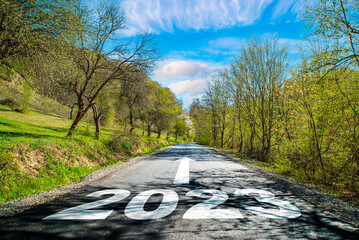 road 2023. Spring landscape near the road in the woods .on the asphalt road written 2023 in front. blue sky with clouds.