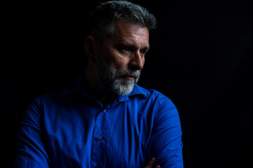 Dramatic portrait of a man in a low key. Studio low key portrait of a mature bearded man wearing a blue shirt. Portrait of an attractive bearded man in low key studio.