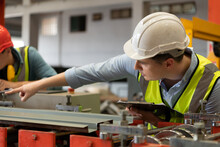 Two Young Engineers Testing And Verifying The Operation Of The Machines Forming Metal Sheet Tiles