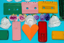 
Creative Art Technological Background With Colorful Retro Cassettes And Phones, Flowers As Decoration Wallpaper And Paper Heart As Copy Space