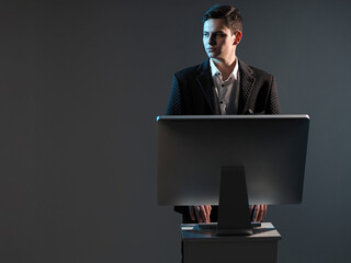 Poster - Man at computer. Businessman stands next to computer. Manager is typing while standing. Businessman with computer on dark background. Male assistant. Successful man types. Place for text