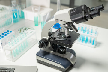Poster - Microscope surrounded by groups of flasks containing blue liquid chemical substance standing on desk in laboratory