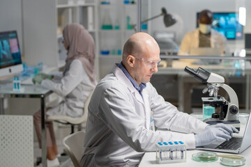 Aufkleber - Mature serious male lab worker in gloves, whitecoat and protective eyeglasses searching for scientific information in the net