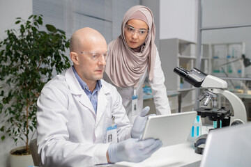 Aufkleber - Two young contemporary virologists discussing online data in laboratory whilemature male scientist pointing at tablet screen