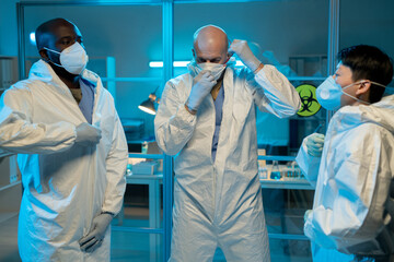 Aufkleber - Three interracial scientists putting on protective coveralls and respirators while going to work with biohazard substances in laboratory