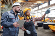 © pressmaster - Young Hispanic female builder in workwear pointing at new equipment while discussing its characteristics with male colleague