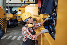 Young Hispanic Female In Protective Helmet, Coveralls And Gloves Checking Engine Of Huge Industrial Machine Before Repairing