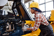 © pressmaster - Young female technician in coveralls and hardhat checking motor of industrial machine while working in large modern factory
