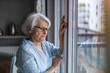 © pikselstock - Senior woman looking out of window at home