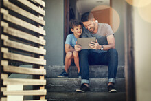 Teaching His Little Guy About An Online World. Shot Of A Father And Son Using A Digital Tablet Together On The Front Steps Of Their Home.