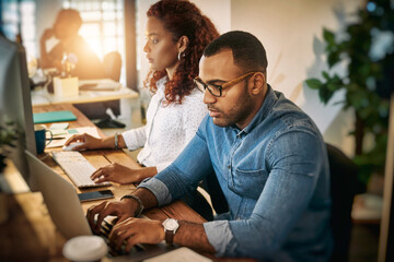 Poster - Putting productivity first. Shot of a young businessman using a laptop with his colleague next to him during a late night at work.